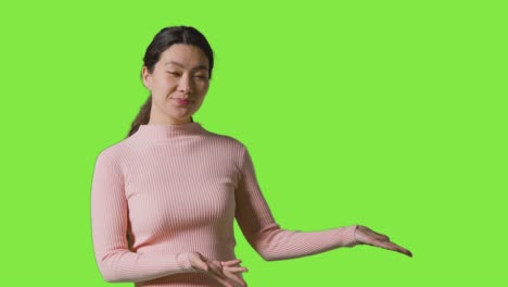 Portrait-Of-Woman-Presenting-Or-Demonstrating-Item-Against-Green-Screen-Smiling-At-Camera
